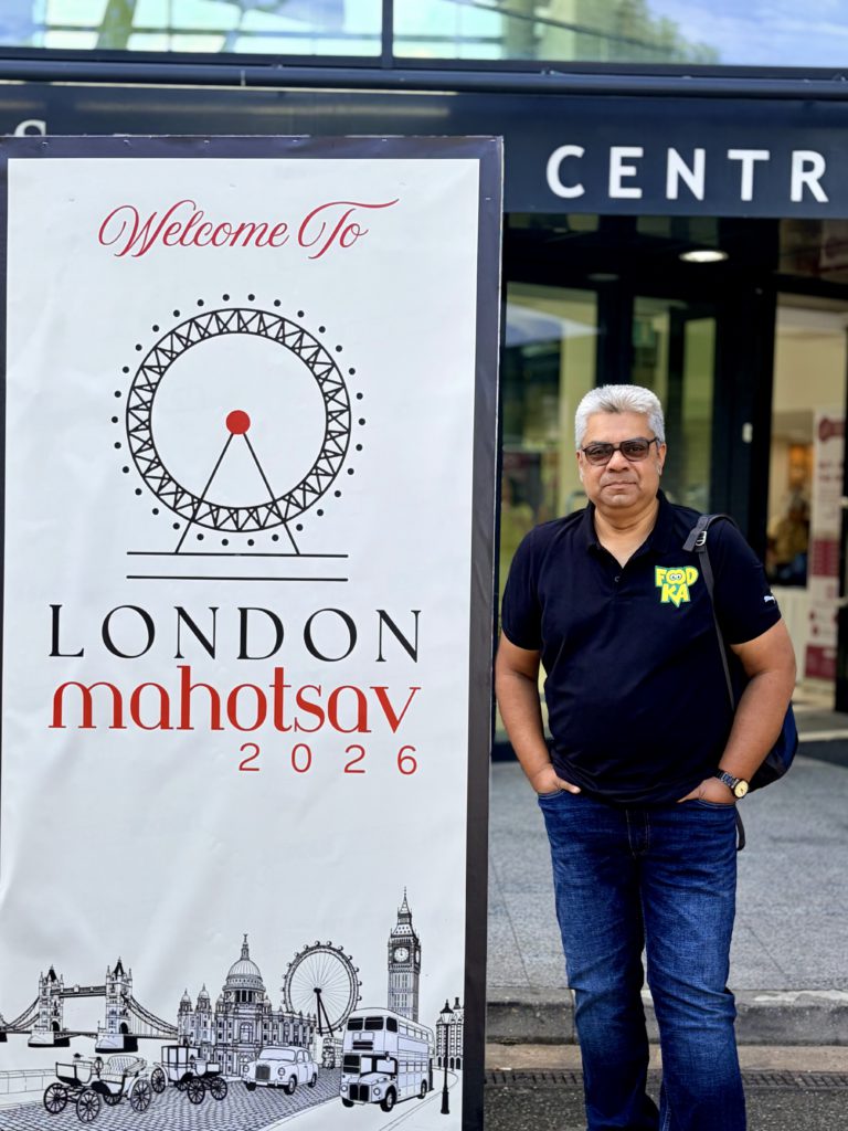 IMG_1186 (1) - Social Nation Man in a dark polo stands beside a tall banner reading'Welcome To London mahotsav 2026' with a ferris wheel graphic on the banner.