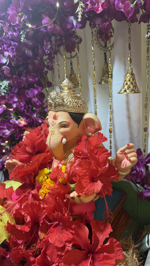 Ganesha - Social Nation Statue of the Hindu god Ganesha with a jeweled crown, red flower garlands, and yellow blooms among purple flowers.